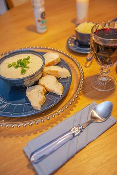 a plate with bread and soup on it next to a glass of red wine,