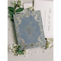 an elegant wedding album with the letter g on it and some white flowers next to it