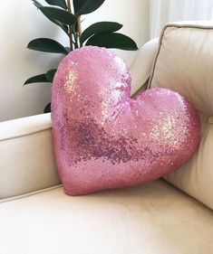 a pink heart shaped pillow sitting on top of a white couch next to a potted plant