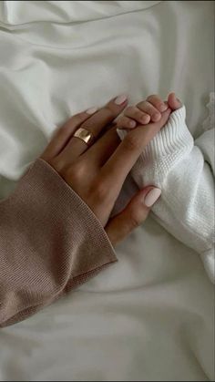 a woman laying in bed with her hands wrapped around the edge of her leg and wearing a pair of gold rings