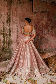 a woman in a pink and gold dress standing next to a wall with peeling paint on it