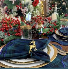 the table is set for christmas dinner with plaid napkins and gold placemats