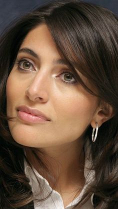 a close up of a person wearing a white shirt and black blazer with silver hoop earrings