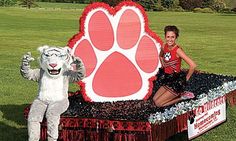 a woman standing next to a mascot on top of a table in the grass with a dog