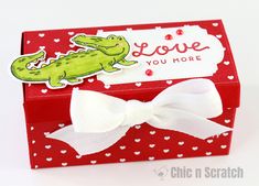 a red box with a white bow and a green alligator on it that says love you more