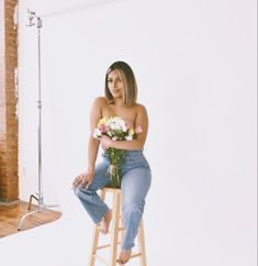 a woman sitting on top of a stool holding flowers