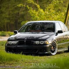 a black car parked on top of a lush green field in front of a forest