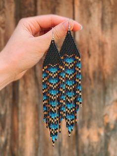 a hand holding up a pair of blue and brown beaded earrings on top of a wooden