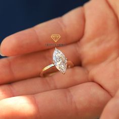 a woman's hand holding a ring with a pear shaped diamond on it,