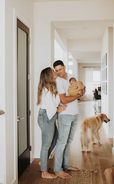 a man and woman holding a baby while standing next to a dog on the floor