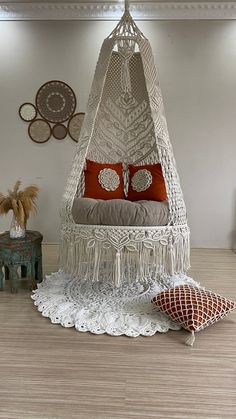 a white hanging chair with two pillows on top of it next to a table and potted plant