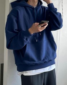 a man in a blue hoodie is holding a cell phone and listening to music