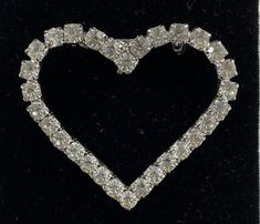 a heart shaped brooch sitting on top of a black velvet case with diamonds in it