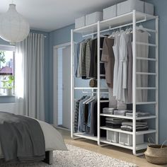 a bedroom with blue walls, white furniture and an open closet that has clothes on it