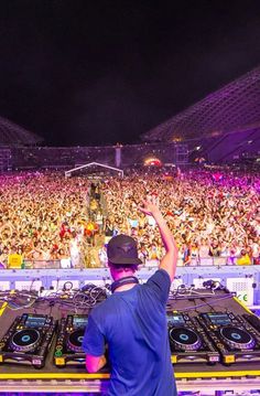 a dj mixing in front of a large crowd at a music festival with his hands up