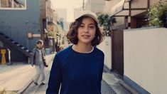 a young man walking down a street next to a woman in a blue shirt and hat