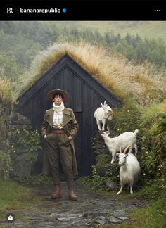 a man standing next to two goats in front of a hut