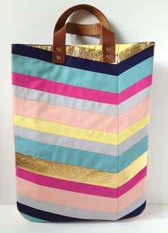 a multicolored striped tote bag hanging on a wall with a wooden handle