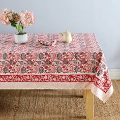 a red and white table cloth with flowers in a vase on it next to a tea pot