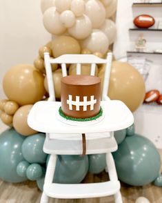 a football cake sitting on top of a white chair in front of balloons and streamers