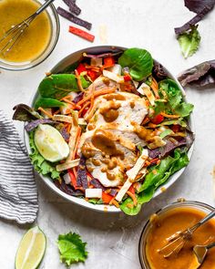 a bowl filled with salad and dressing next to two bowls full of sauces on the side