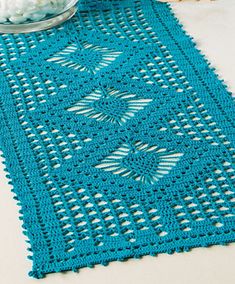 a blue crocheted table runner next to a bowl of cotton