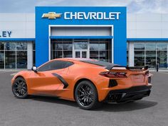 an orange sports car parked in front of a chevrolet dealership