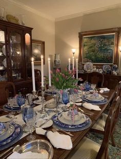 a dining room table is set with blue and white china plates, candles, and flowers