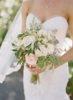 a woman in a wedding dress holding a bridal bouquet with white and pink flowers