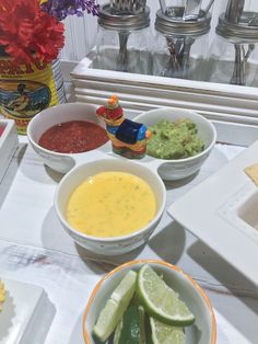 bowls of guacamole, salsa and lime slices on a white tablecloth