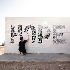 a man kneeling down next to a wall with graffiti on it's side and writing that says hope