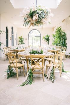 a dining room with tables and chairs set up for a formal function, surrounded by greenery