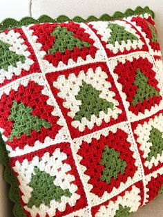 a red and white crocheted christmas pillow with holly decorations on the front, sitting on a couch