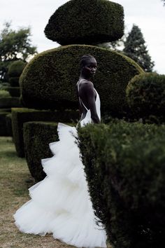 a woman in a white dress standing next to some hedges