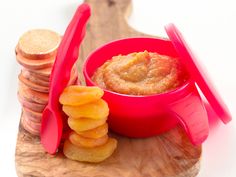 a red bowl filled with food sitting on top of a wooden cutting board next to stacks of crackers