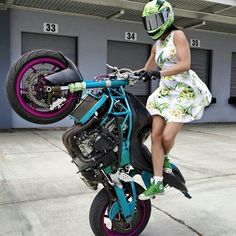 a woman sitting on top of a dirt bike in front of a garage door with purple rims