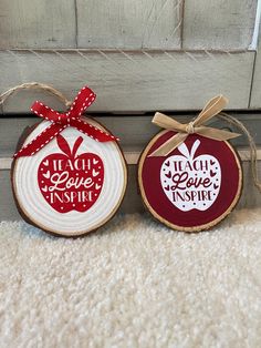 two wood slices with red and white designs on them, one has an apple and the other says teach love inspire