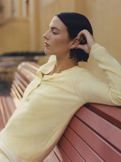 a woman sitting on top of a red bench next to a wooden wall and wearing a yellow sweater