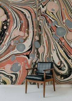 a chair sitting in front of a large wall with an abstract painting on it's side