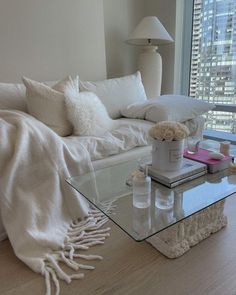 a living room filled with furniture and a glass coffee table covered in white blankets on top of a hard wood floor