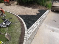 a garden being worked on with tools and gravel in the foreground, next to a driveway