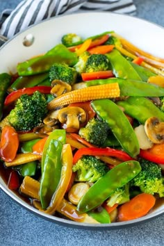 stir fry vegetables in a white pan on a blue counter top with a striped napkin