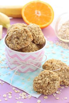 some cookies in a pink and white bowl next to an orange slice on a table