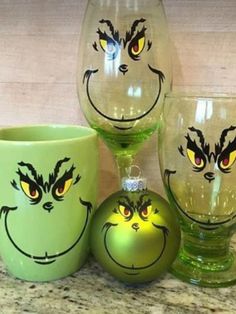 three glasses with faces painted on them sitting on a counter top next to a green ornament