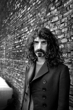 a man with long hair standing next to a brick wall