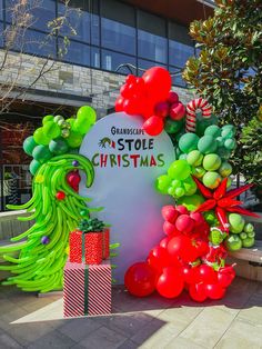 an outdoor christmas display with balloons and presents in front of a building that has a large sign on it