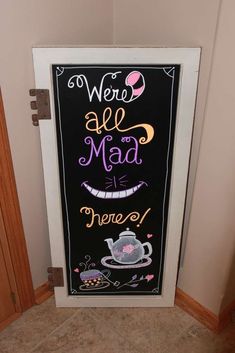 a chalkboard sign that says we're all mad and there is a teapot on it