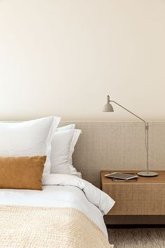 a bed with white sheets and pillows next to a lamp on a nightstand in a bedroom