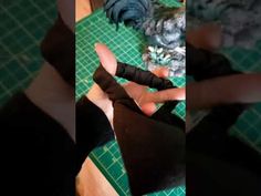 someone is cutting up something with scissors on a green table top and another person's feet are visible in the background