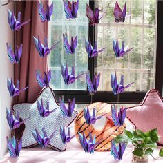 purple origami birds are flying in the air next to a potted plant